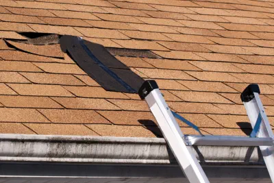 A ladder leans against a damaged roof that needs Burroughs Roofing to repair it.