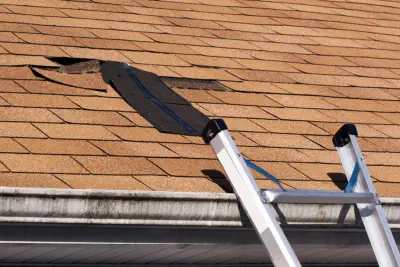 A ladder leans against a damaged roof that needs Burroughs Roofing to repair it.